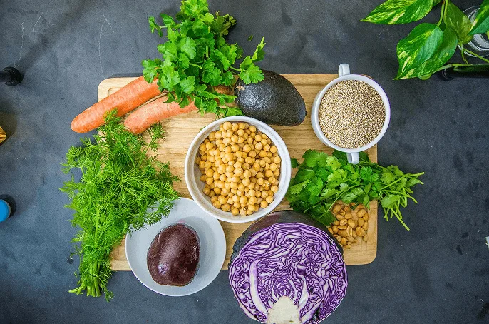 Colorful fresh vegetables, legumes, and grains on wooden board including carrots, avocado, chickpeas, and cabbage