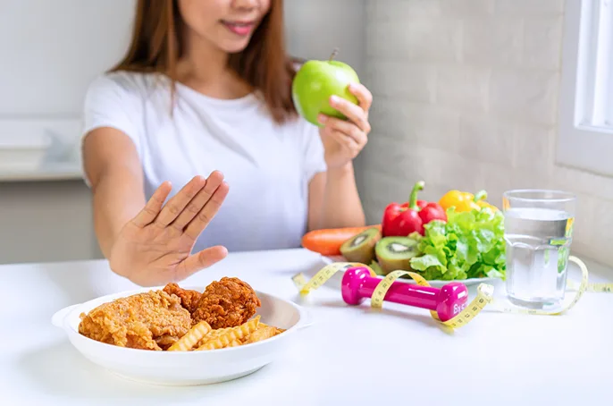 Healthy choice over fried food: person picks apple with fruits, veggies, water, and fitness items on table