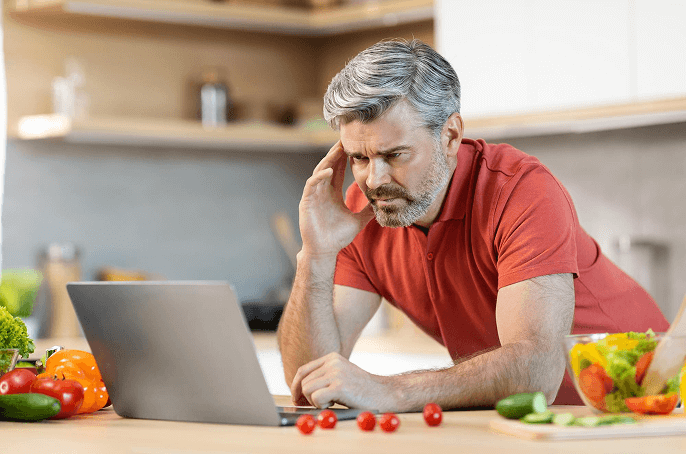 Man in kitchen with laptop and fresh vegetables, researching The Surprising Truth About Diets